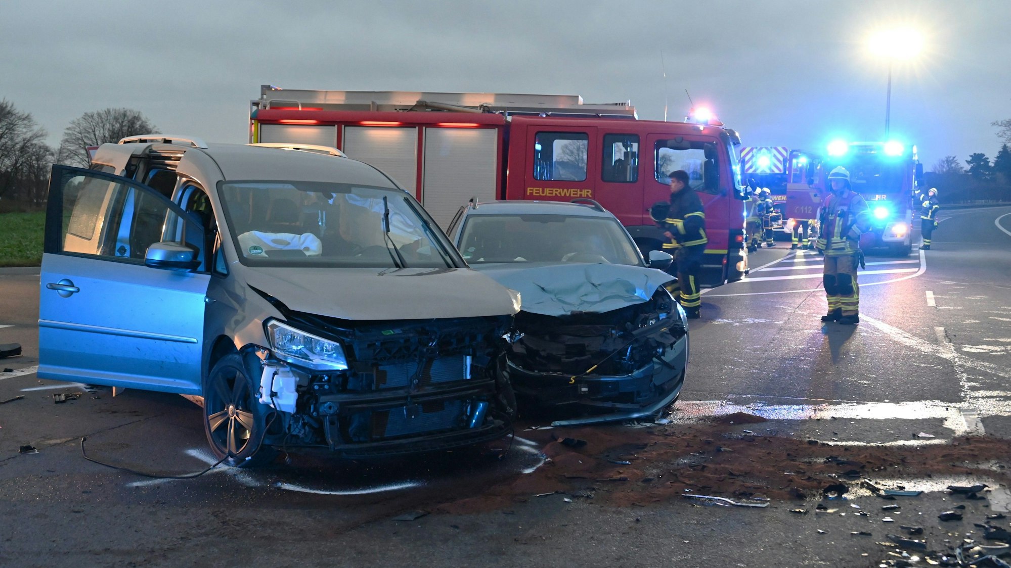 Zwei beschädigte Fahrzeuge stehen quer auf der Fahrbahn. Im Hintergrund Feuerwehrfahrzeuge und Einsatzkräfte.