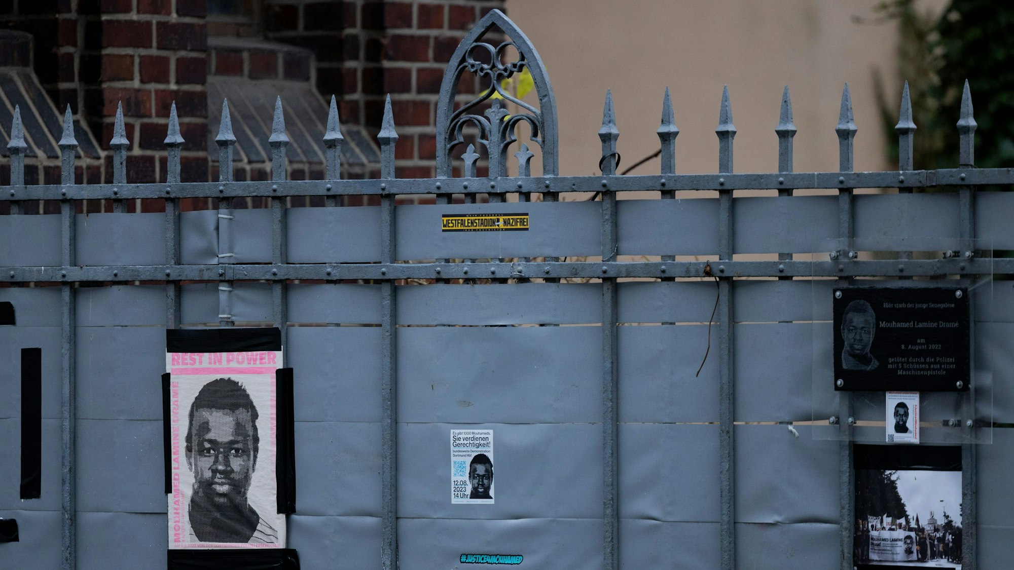 Dortmund: Plakate und eine Plakette erinnern am Tatort (hinter dem Zaun) an den 16-jährigen Senegalesen Mouhamed Drame. Am 19.12.2023 begann der Prozess nach tödlichen Polizeischüssen auf einen jungen Flüchtling. Der Jugendliche aus dem Senegal war am 8. August 2022 auf dem Gelände einer Jugendhilfeeinrichtung erschossen worden.