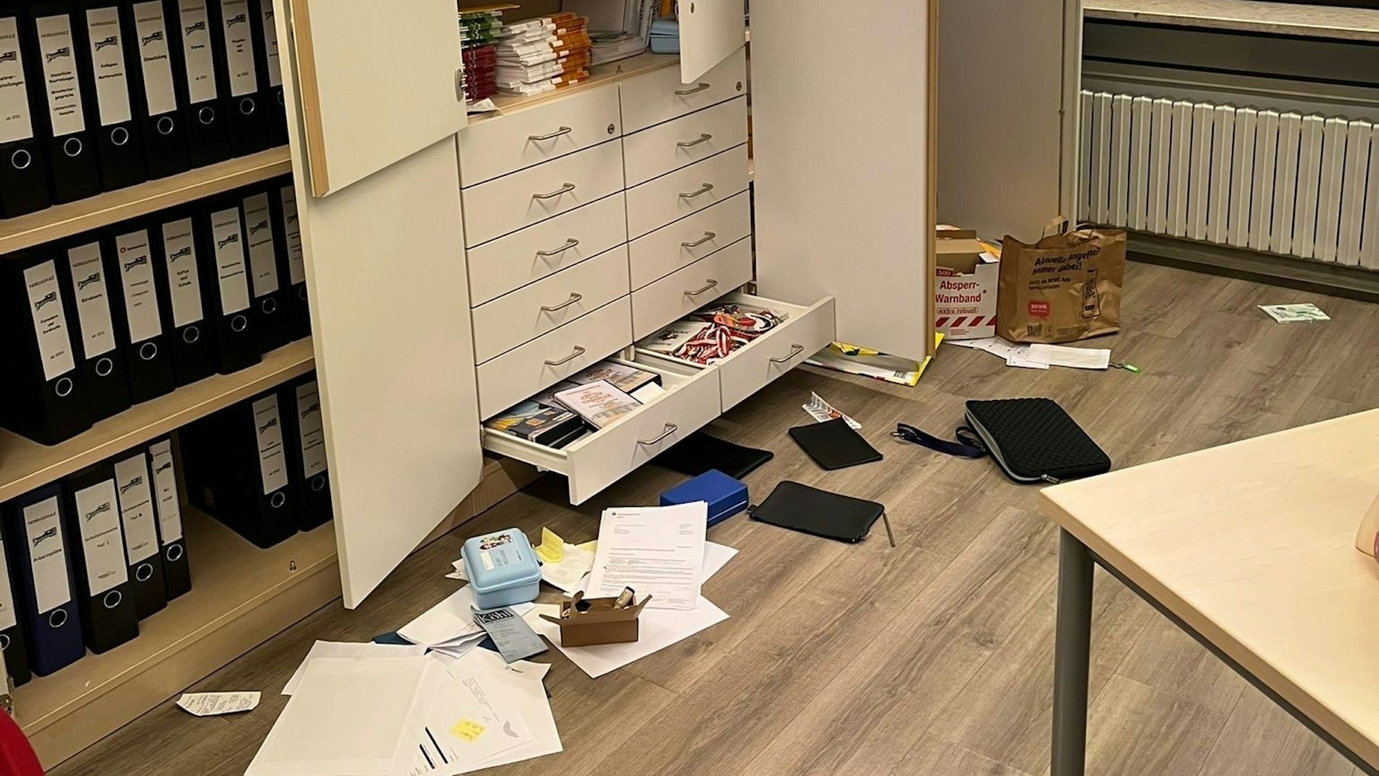 Zu sehen ist ein aufgebrochener Schrank, vor dem Gegenstände liegen.