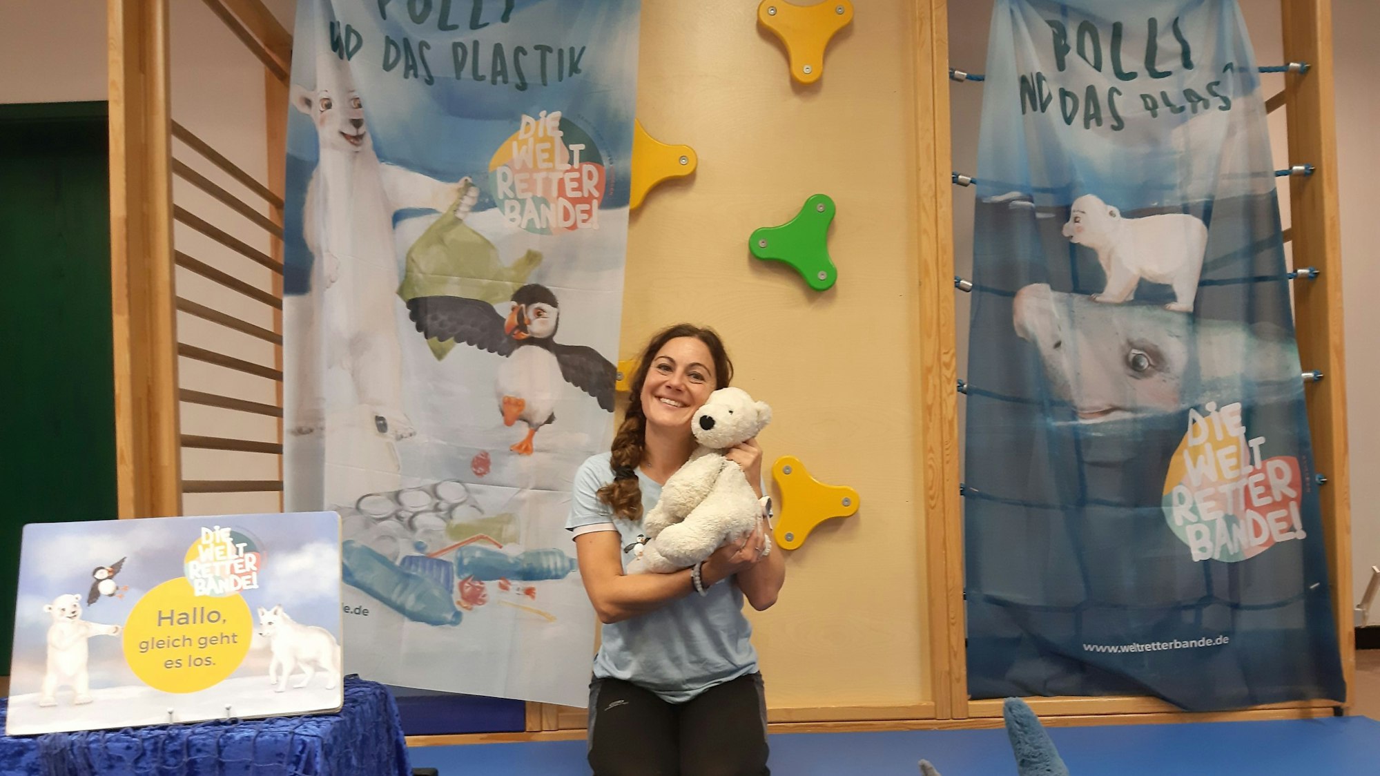 Silke Heiser ist in einer Turnhalle und hält einen Kuscheltier-Eisbären auf dem Arm.