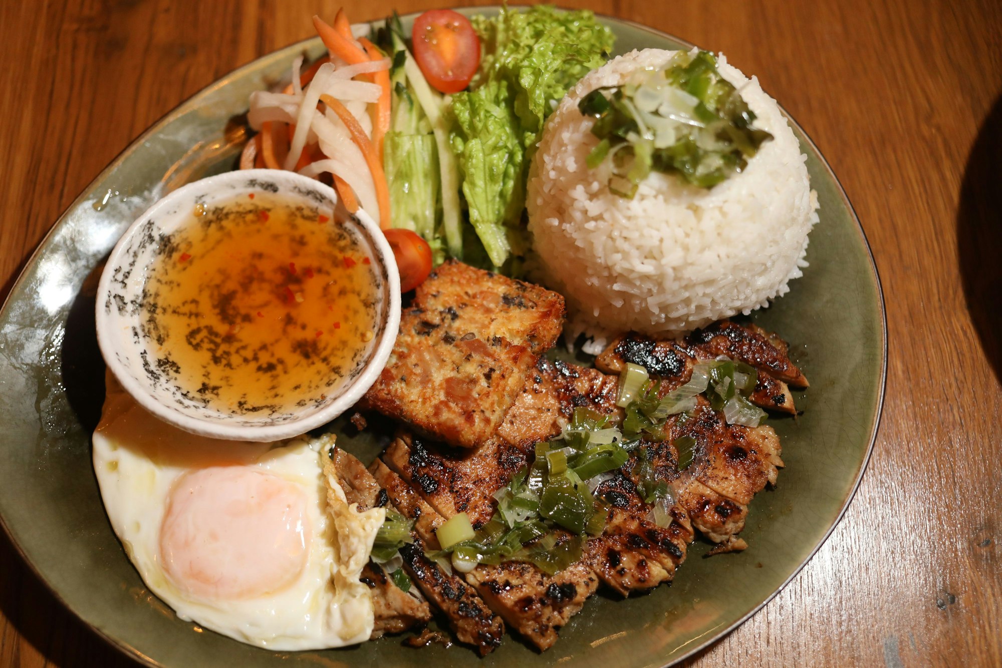 Ein Tellergericht mit in Scheiben geschnittenem Fleisch, Reis, Salat und Spiegelei ist zu sehen. In einem Schälchen die Vinaigrette.