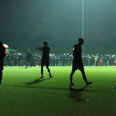 Die Spieler machen sich im Schatten warm. Ein Teil der Flutlichtanlage funktioniert bereits wieder.