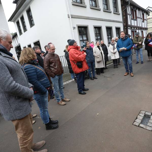 Mehrere Menschen auf einer Straße, am Rand liegen Messingsteine, die in die Straße eingesetzt werden sollen.