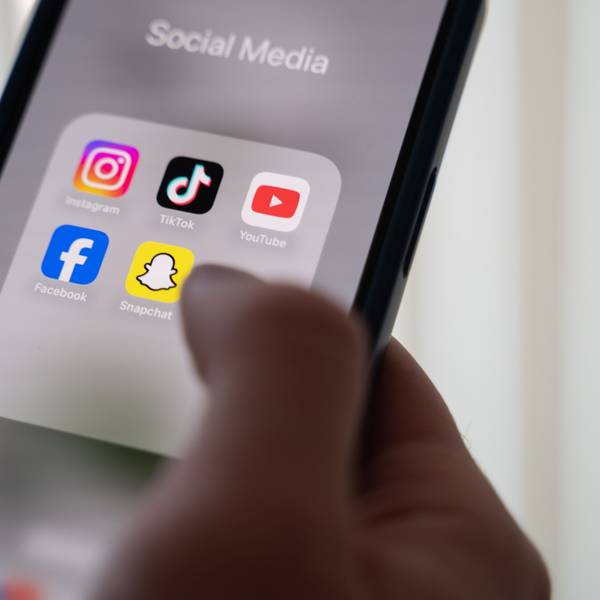 Eine Frau hält ein Smartphone, auf dessen Display verschiedene Social Media Apps angezeigt werden.