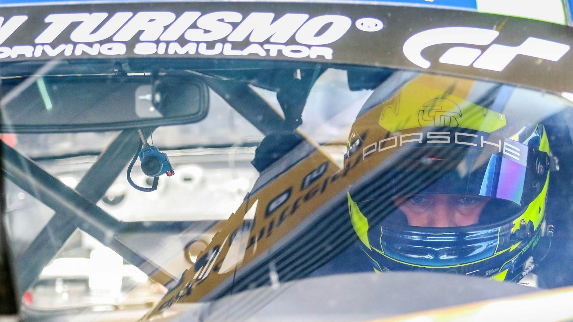 Tobias Müller sitzt im Auto, trägt seinen Helm mit offenem Visier, auf der Windschutzscheibe spiegelt sich die Boxengasse.