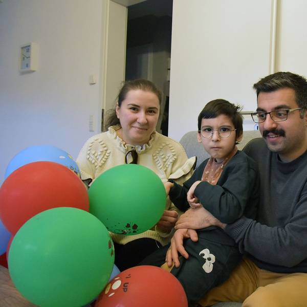 Ein Kind auf dem Schoß seines Vaters, daneben auf dem Sofa die Mutter, im Vordergrund bunte Ballons.