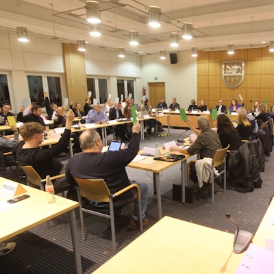 In einem Sitzungssaal heben Menschen rotze und grüne Karten in die Höhe.