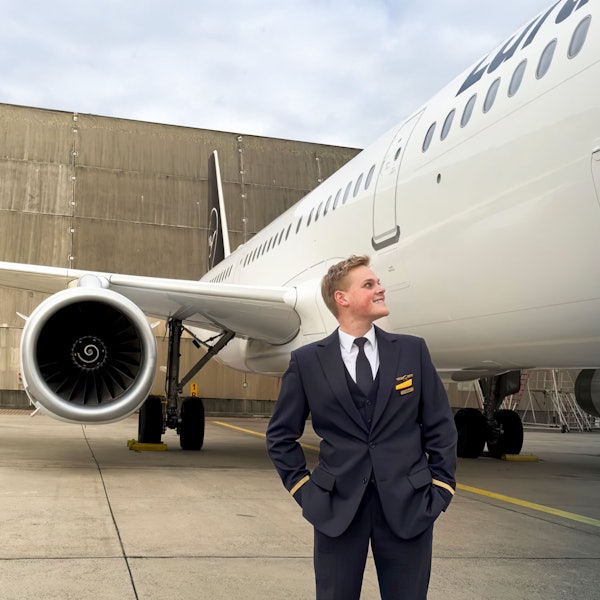 Alex Böhmer steht in seiner Uniform auf einem Rollfeld und blickt auf ein Flugzeug, das neben ihm steht.