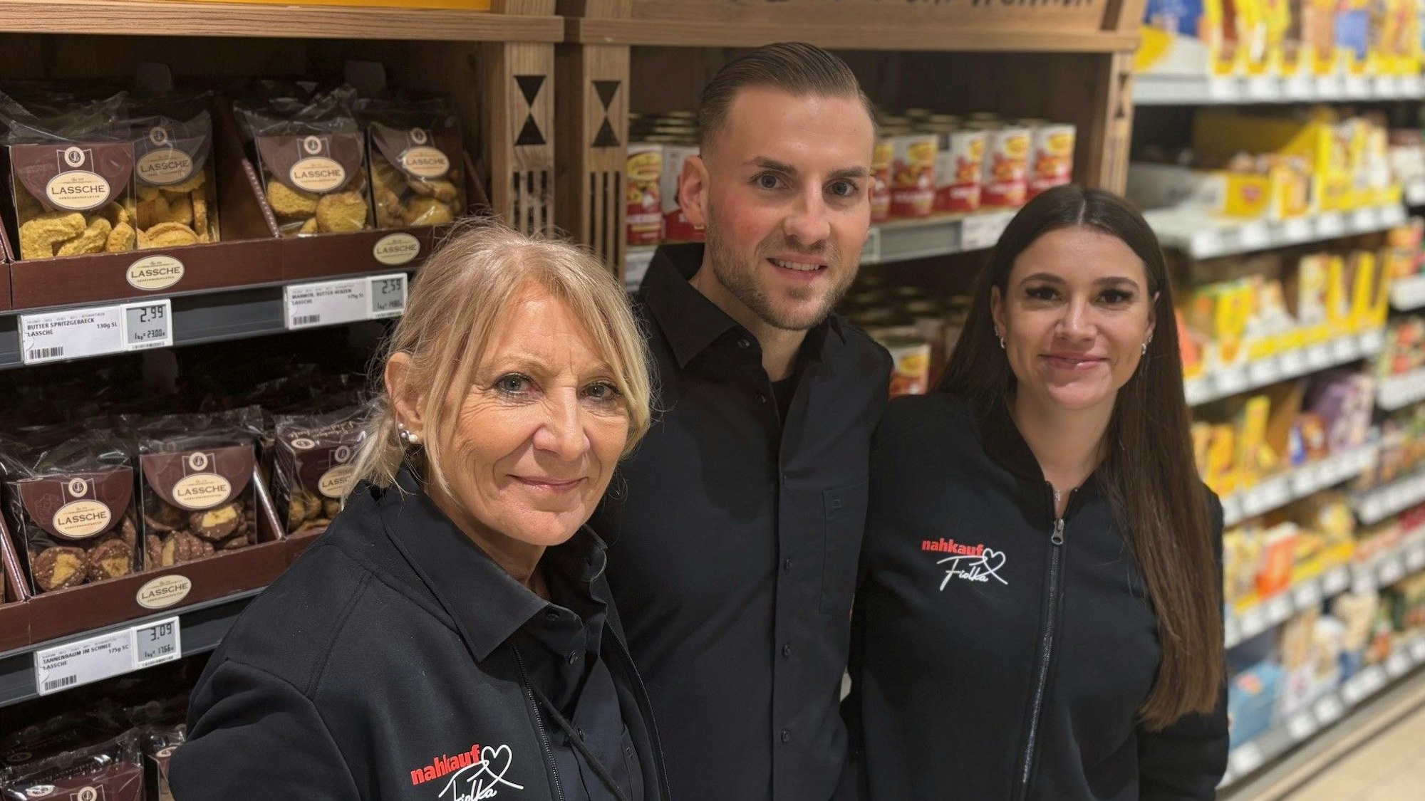 Auf dem Bild ist ein Mann mit seiner Mutter und seiner Freundin vor einem Supermarktregal zu sehen.