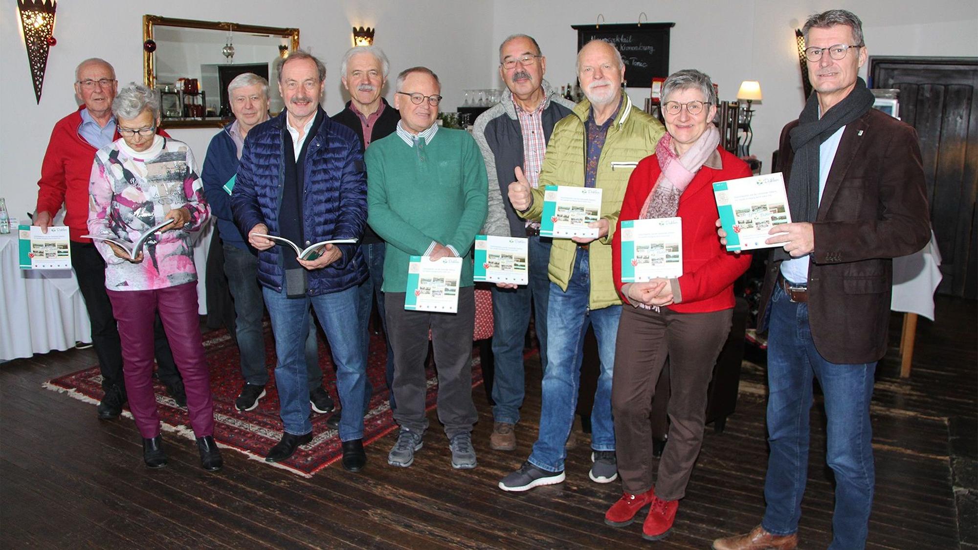 Eine Gruppe von Männern und Frauen posiert für ein Foto, sie halten ein Buch in den Händen.
