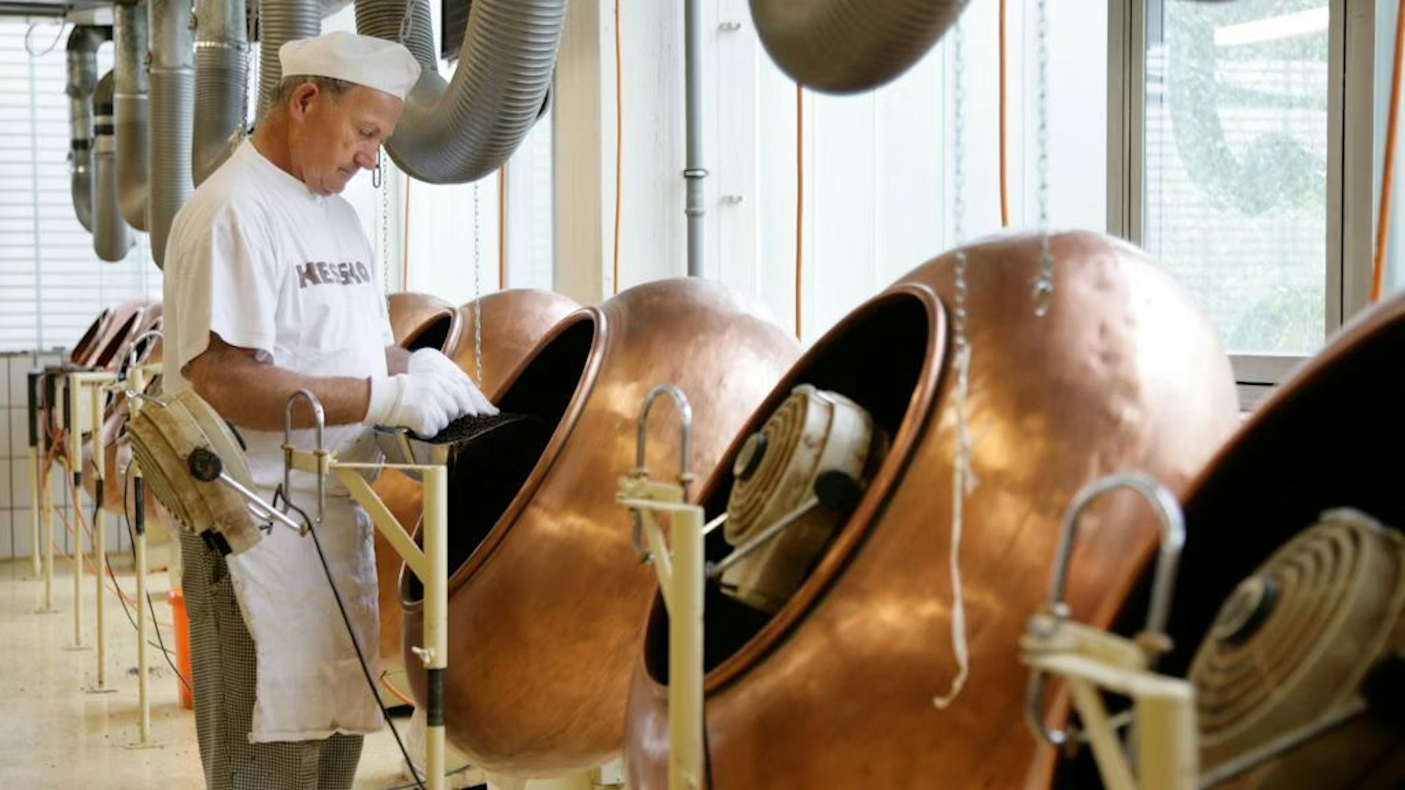 Ein Mann arbeitet an einer runden Maschine in dem Bonner Süßwarenunternehmen Kessko. Er trägt weiße Schutzkleidung.