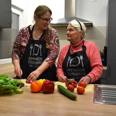 Gemeinsam schnippeln Leiterin Maike Wittenburg und die Ehrenamtliche Helga Herzog in einer Küche Gemüse für einen bunten Salat.