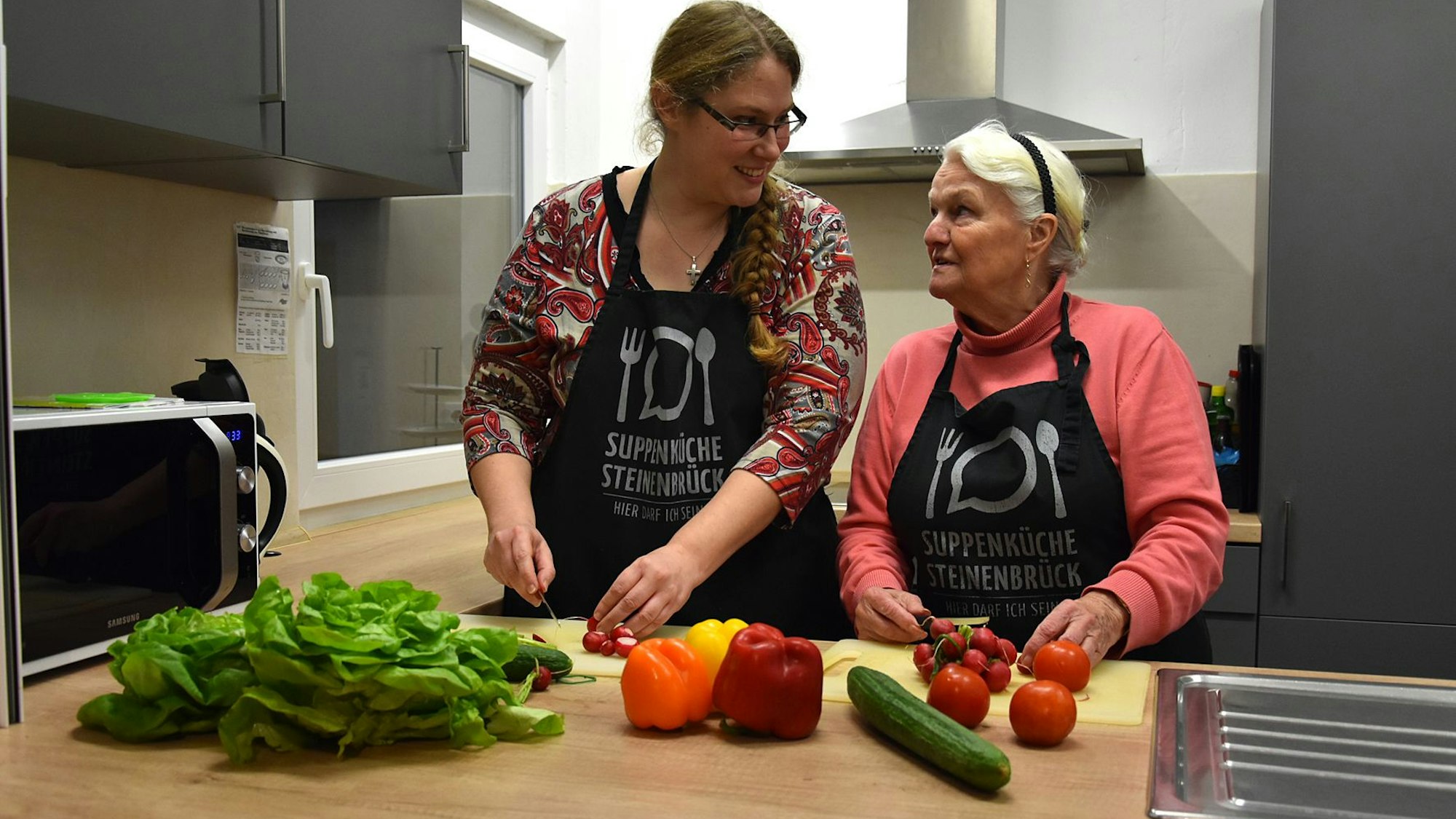 Gemeinsam schnippeln Leiterin Maike Wittenburg und die Ehrenamtliche Helga Herzog in einer Küche Gemüse für einen bunten Salat.