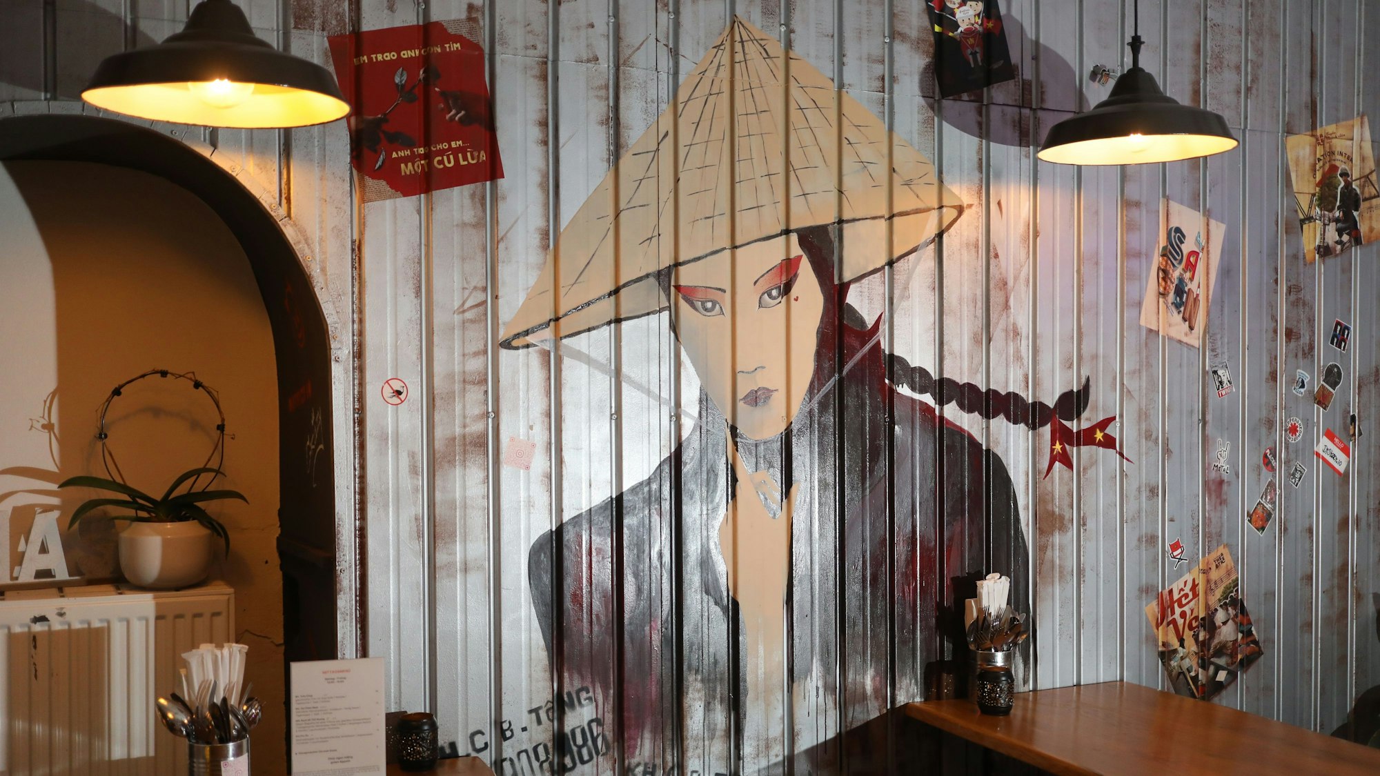 Auf einer Wand ist ein Graffito zu sehen, dass eine Frau mit traditionellem vietnamesischen Kegelhut zu sehen.
