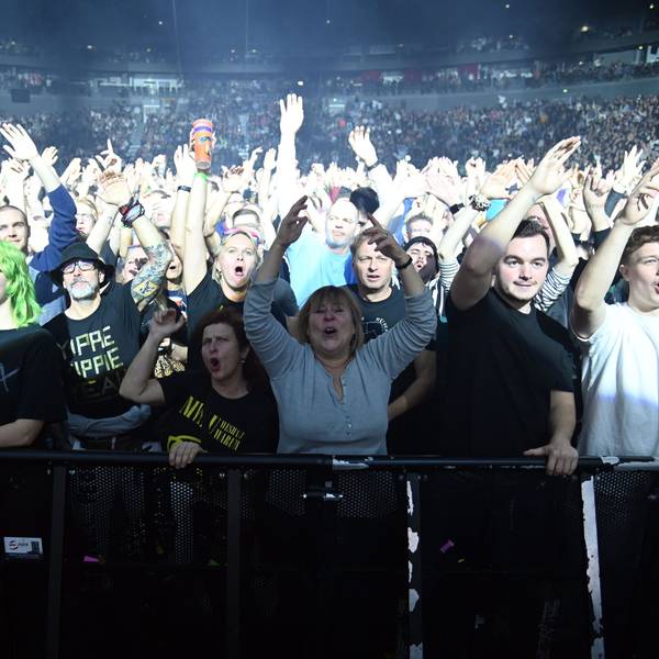 Zuschauer stehen in der ersten Reihe bei einem Konzert in der Lanxess-Arena und heben die Arme in die Luft.