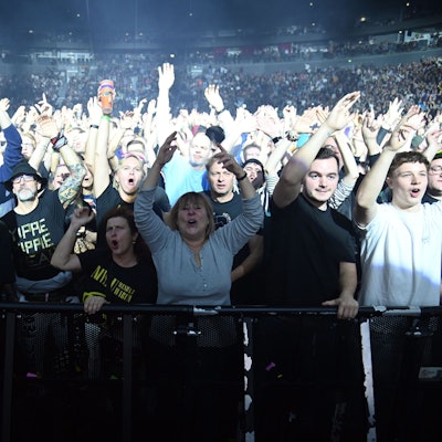 Zuschauer stehen in der ersten Reihe bei einem Konzert in der Lanxess-Arena und heben die Arme in die Luft.