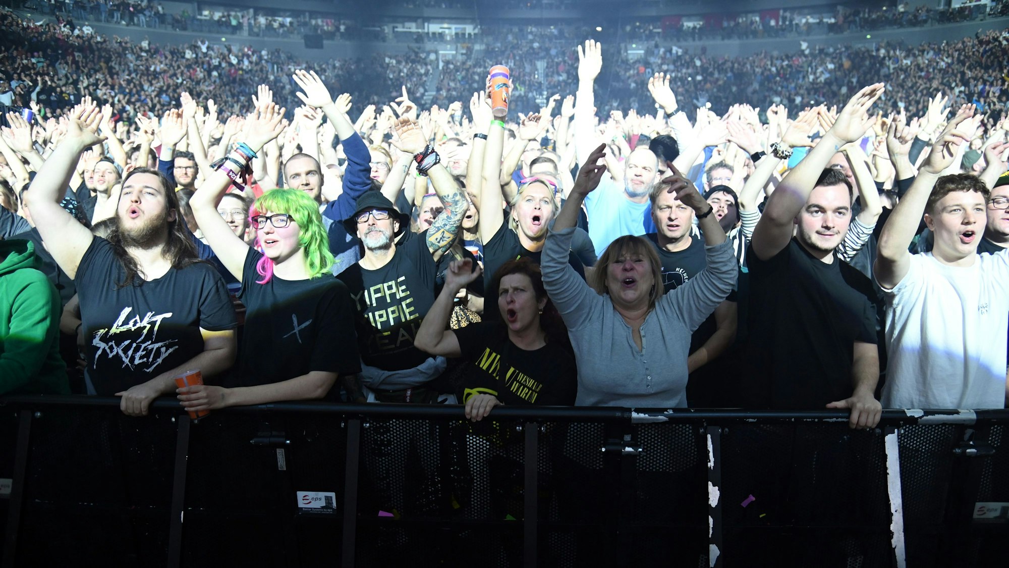 Zuschauer stehen in der ersten Reihe bei einem Konzert in der Lanxess-Arena und heben die Arme in die Luft.