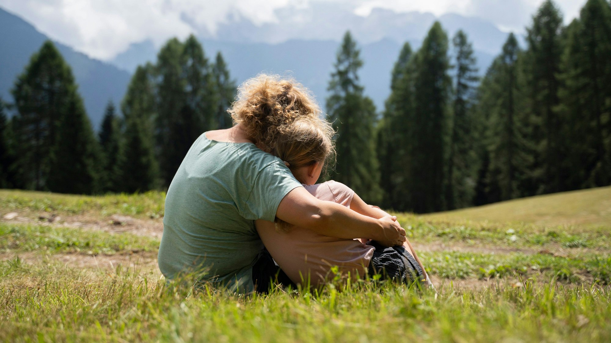 Mutter und Tochter sitzen auf einer Wiese in den Bergen.