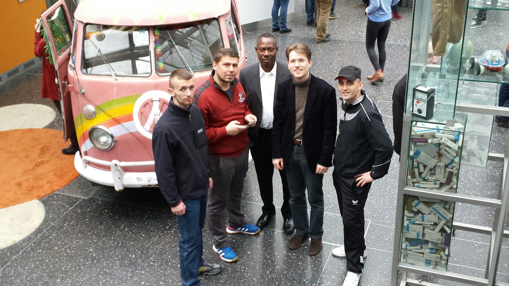 Mehrere junge Männer stehen vor einem bunt bemalten alten VW-Bus.