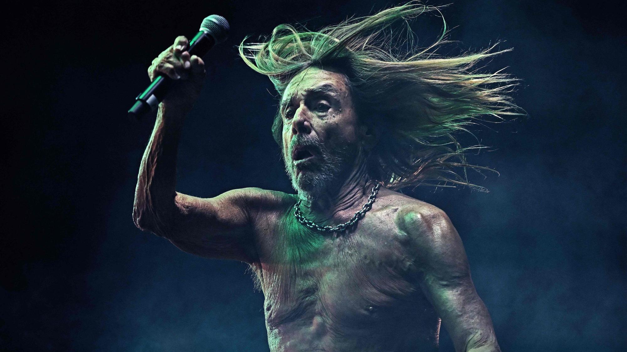 Iggy Pop hält ein Mikrofon in der Hand und bewegt sich.