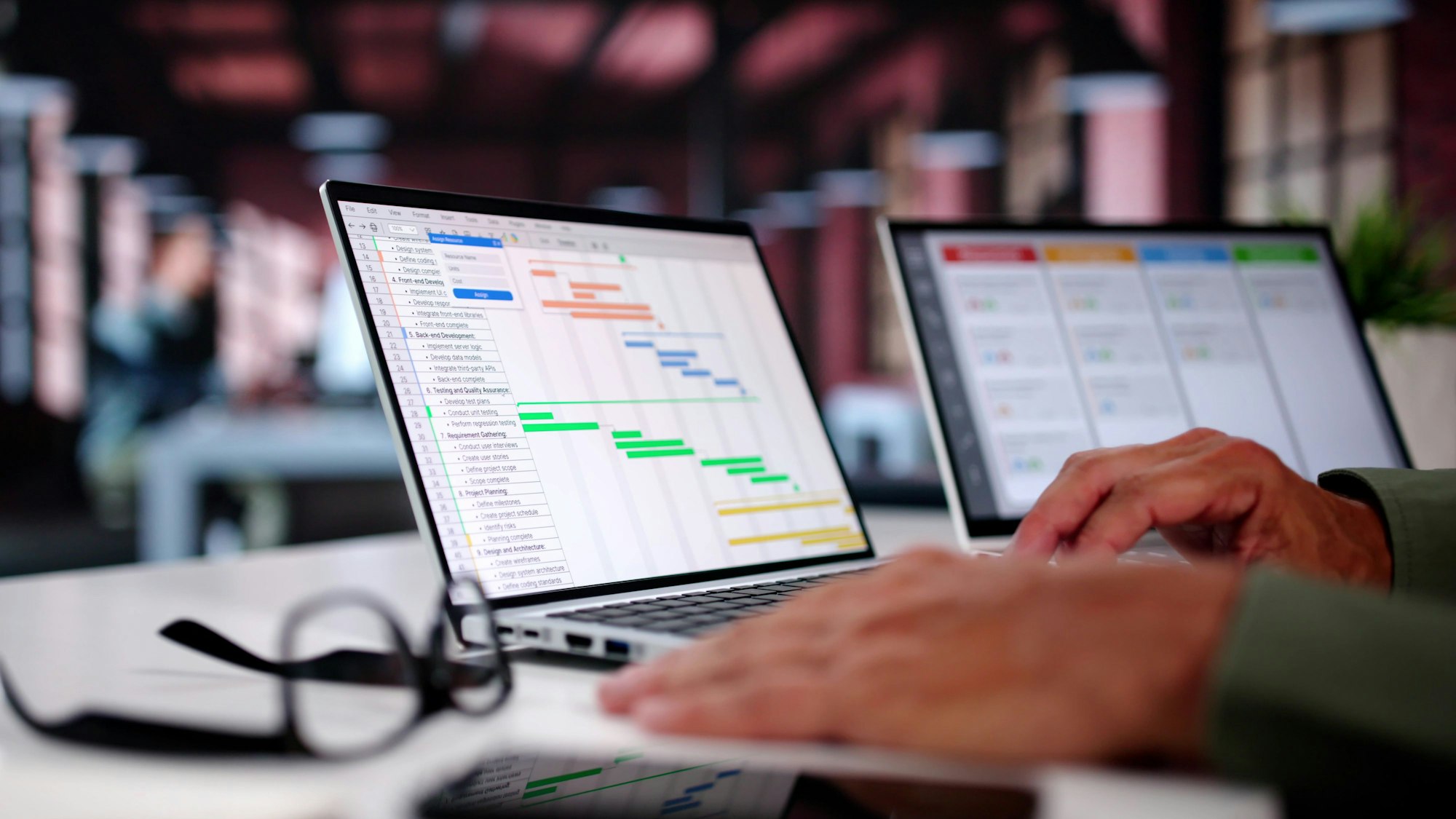 Eine Person sitzt an einem Schreibtisch, vor ihr stehen zwei Laptops, auf denen virtuelle Kalender angezeigt werden