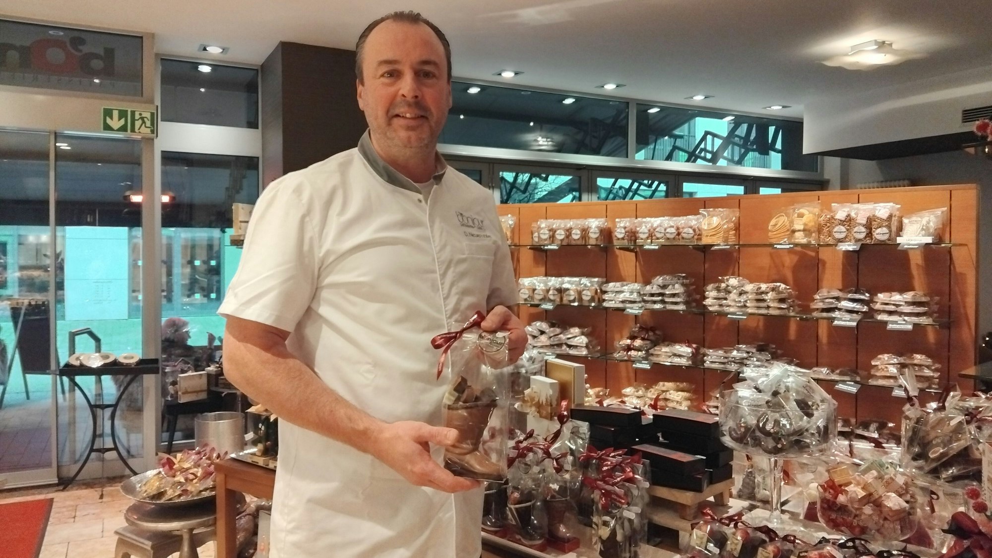 Ein Mann steht in einem Café und hält einen Schokoladenstiefel, im Hintergrund sieht man weitere Schokoladenprodukte.