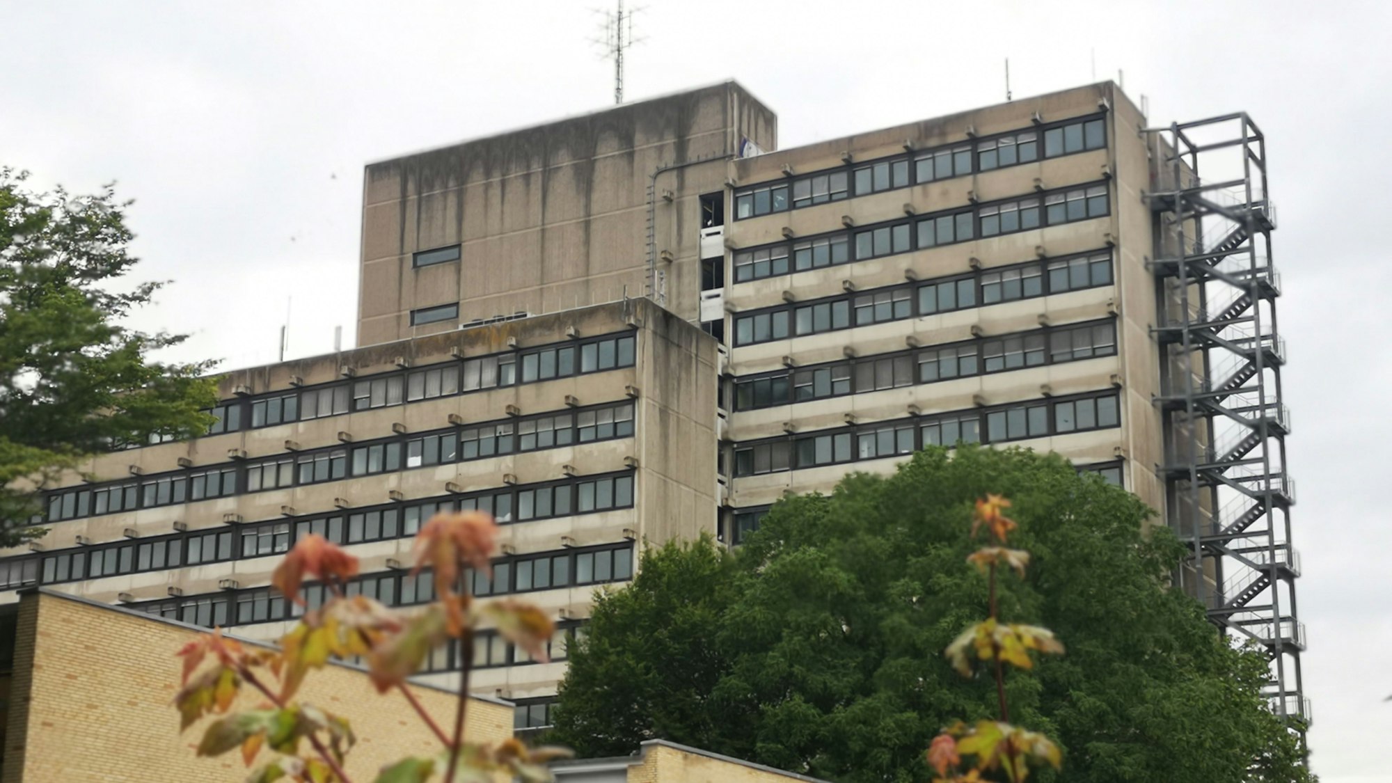Ein grau-braunes Betonhochhaus mit vielen Fenstern vor einem grauen Himmel.