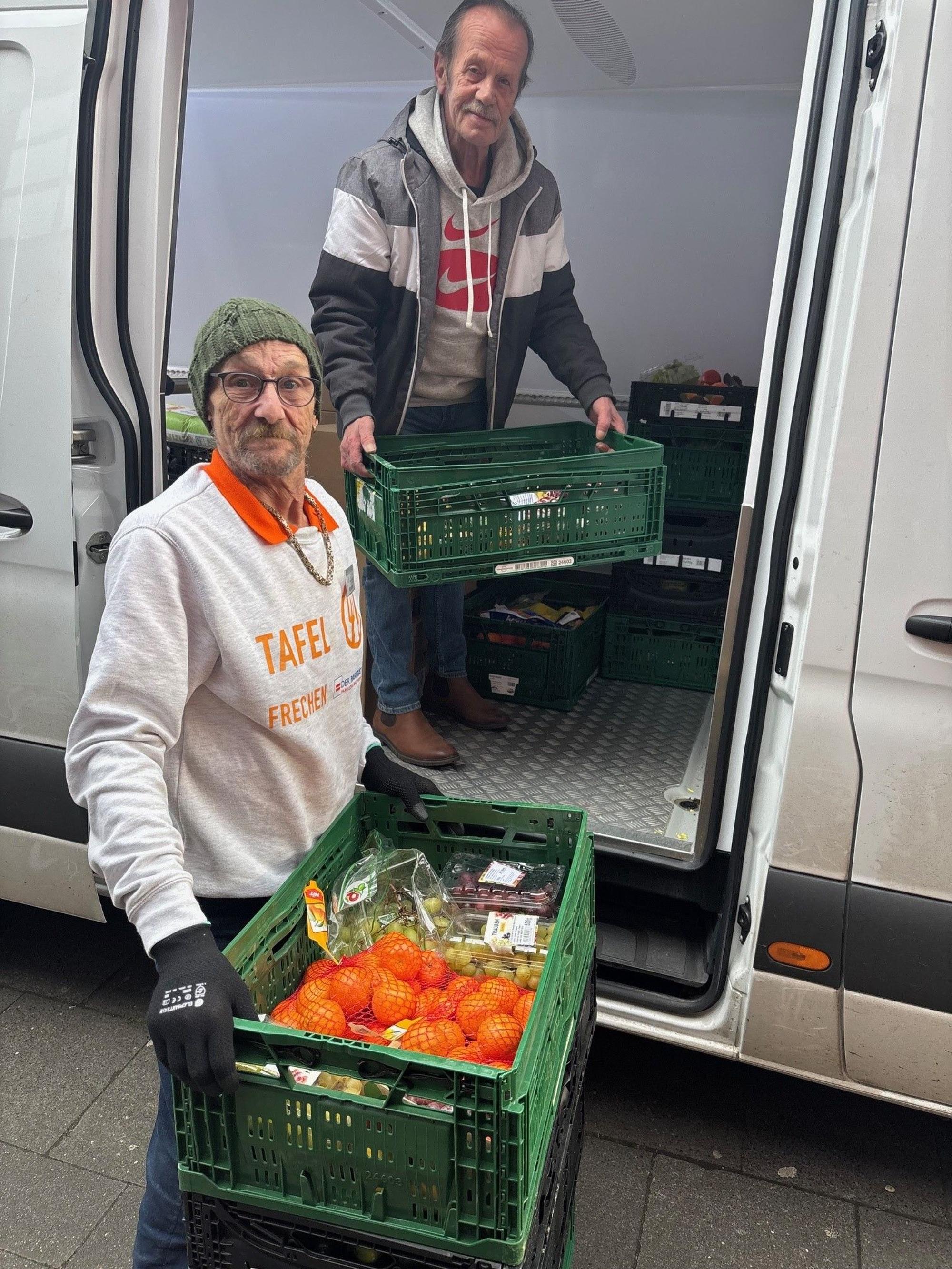 Auf dem Bild sind zwei Männer zu sehen, die Lebensmittel aus einem Transporter heben.