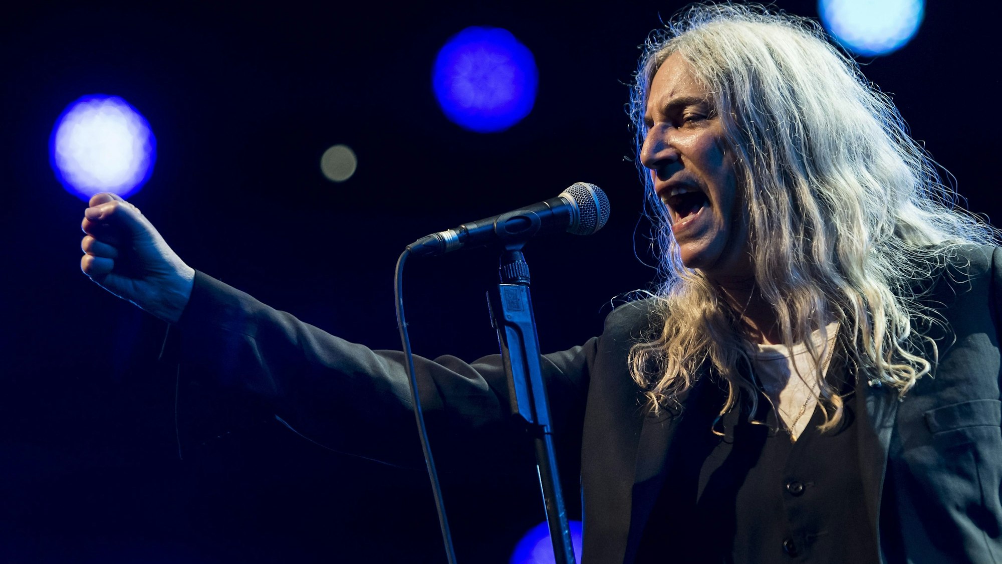Patti Smith singt ins Mikrofon und streckt die Faust nach vorne.