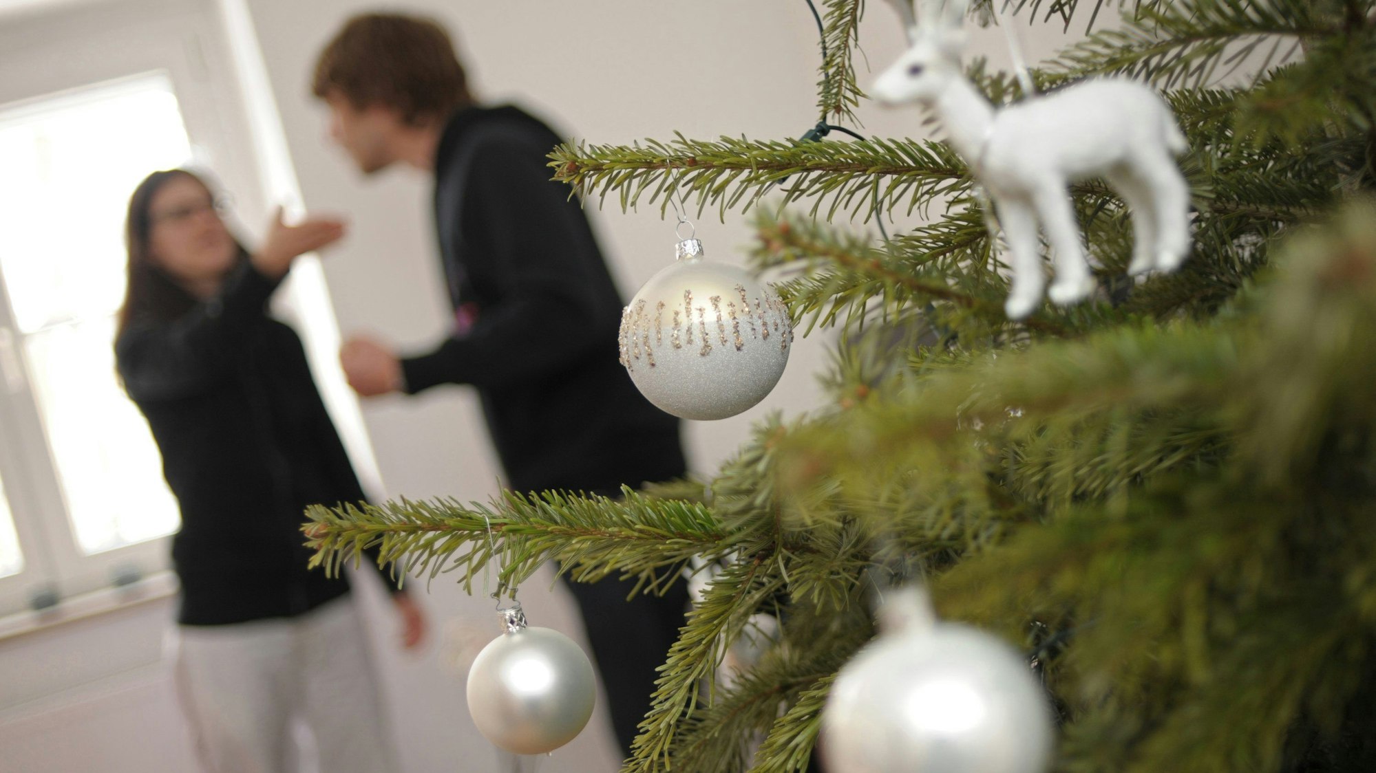 Hinter einem Weihnachtsbaum streiten sich zwei Personen.