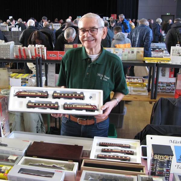 Ein 83 Jahre alter Mann hält eine offene Packung mit Modellbahnwagen in den Händen.