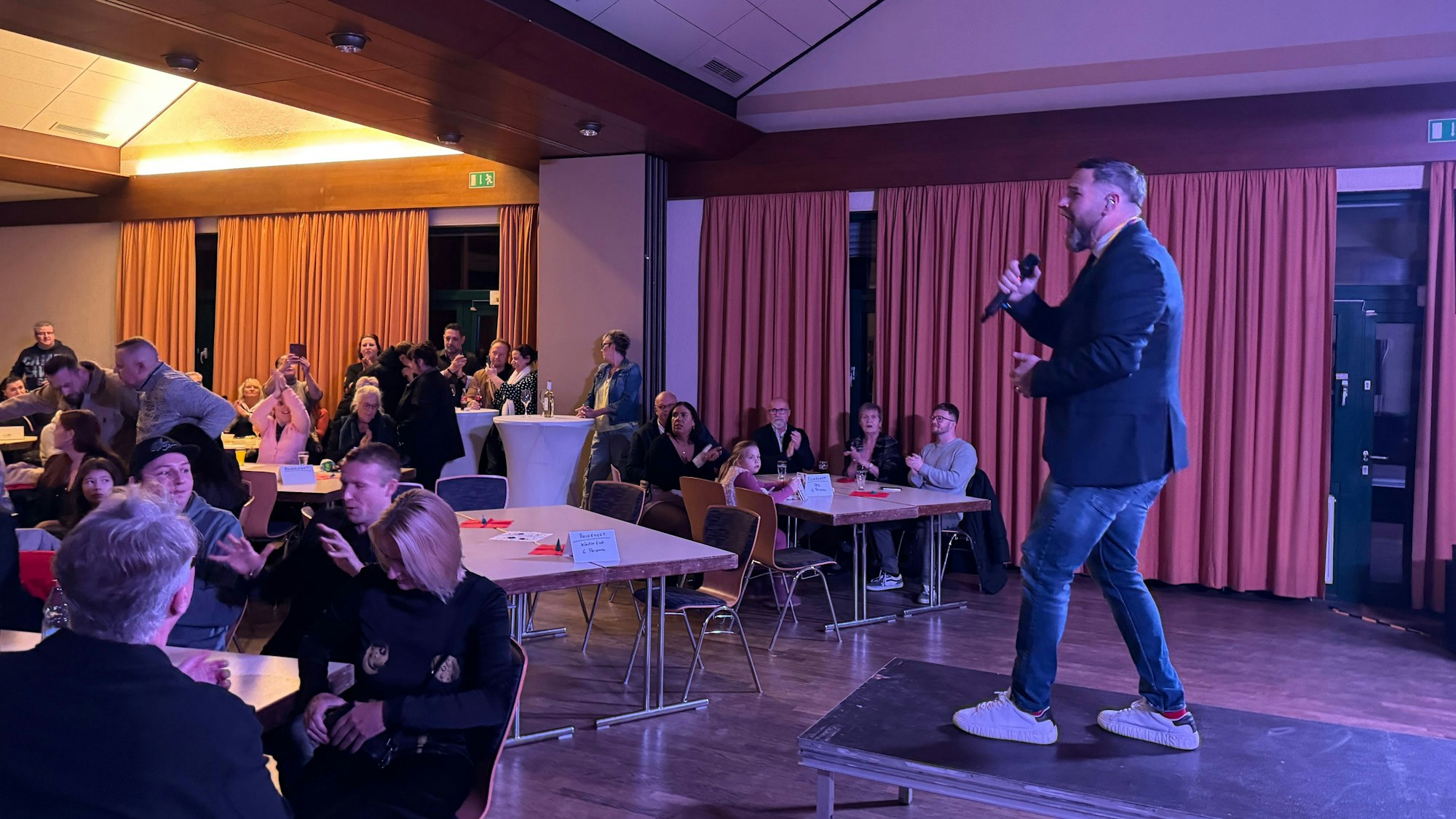 Ein Mann steht mit einem Mikrofon auf einer Bühne und hält eine Ansprache.