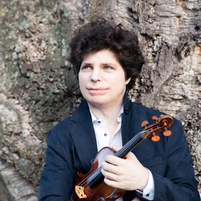 Der Geigen-Virtuose Augustin Hadelich steht vor einem Baum.