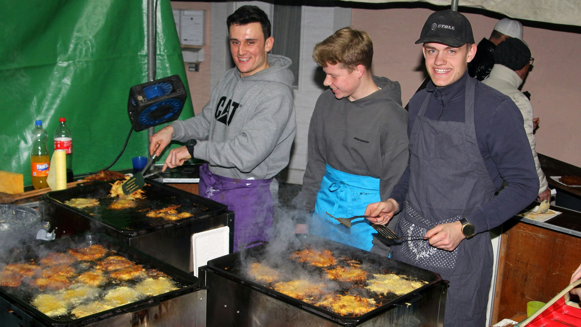 Auf dem Bild sind drei junge Männer zu sehen, die Reibekuchen herstellen.