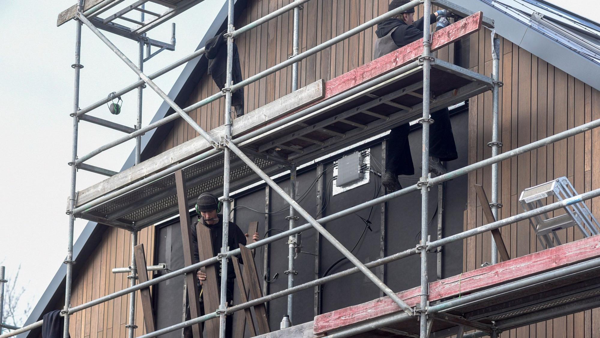 Auf dem Bild ist ein eingerüstetes Haus mit Handwerkern zu sehen.