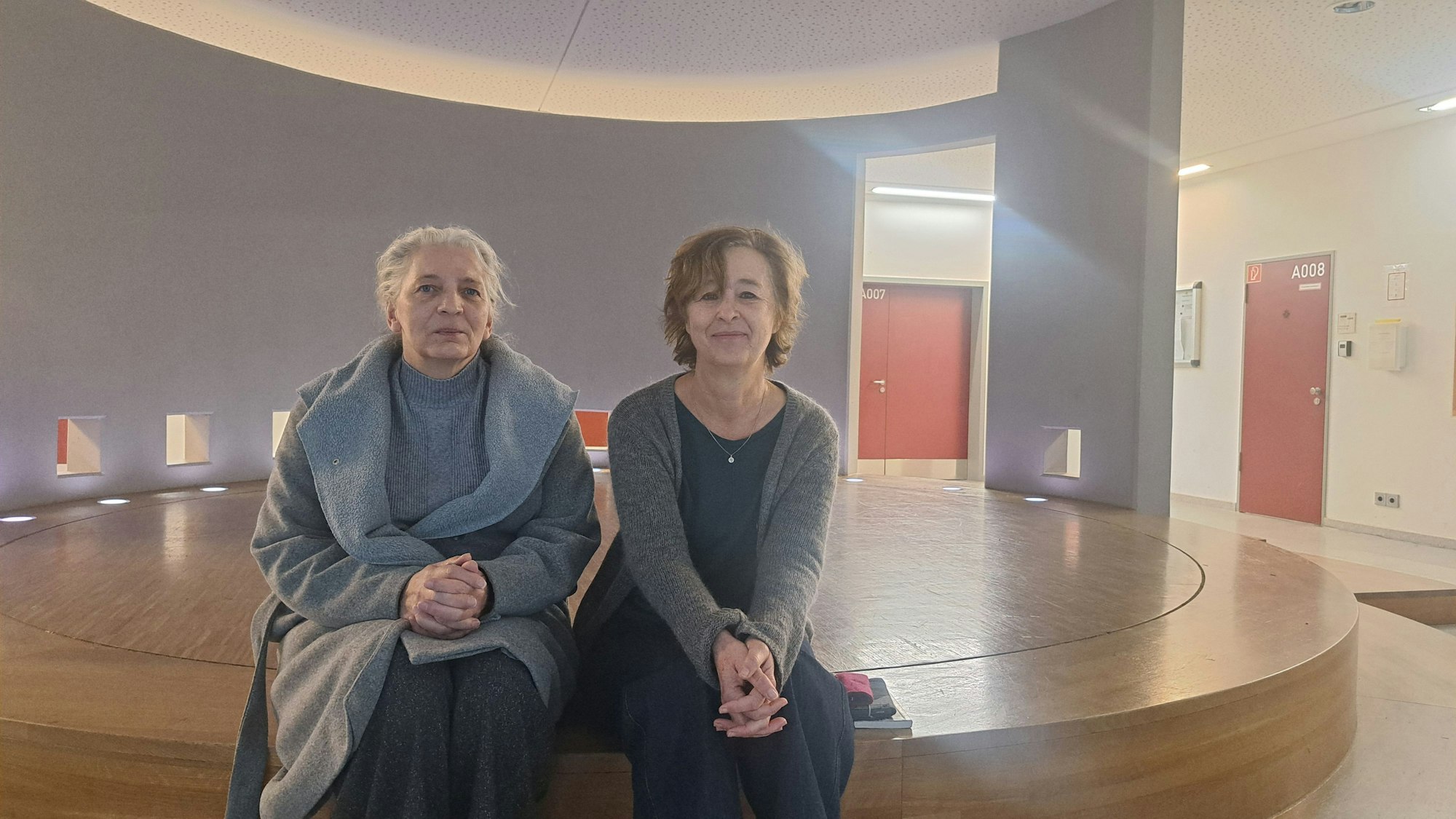 Zwei Frauen sitzen auf einer runden Holzbühne.