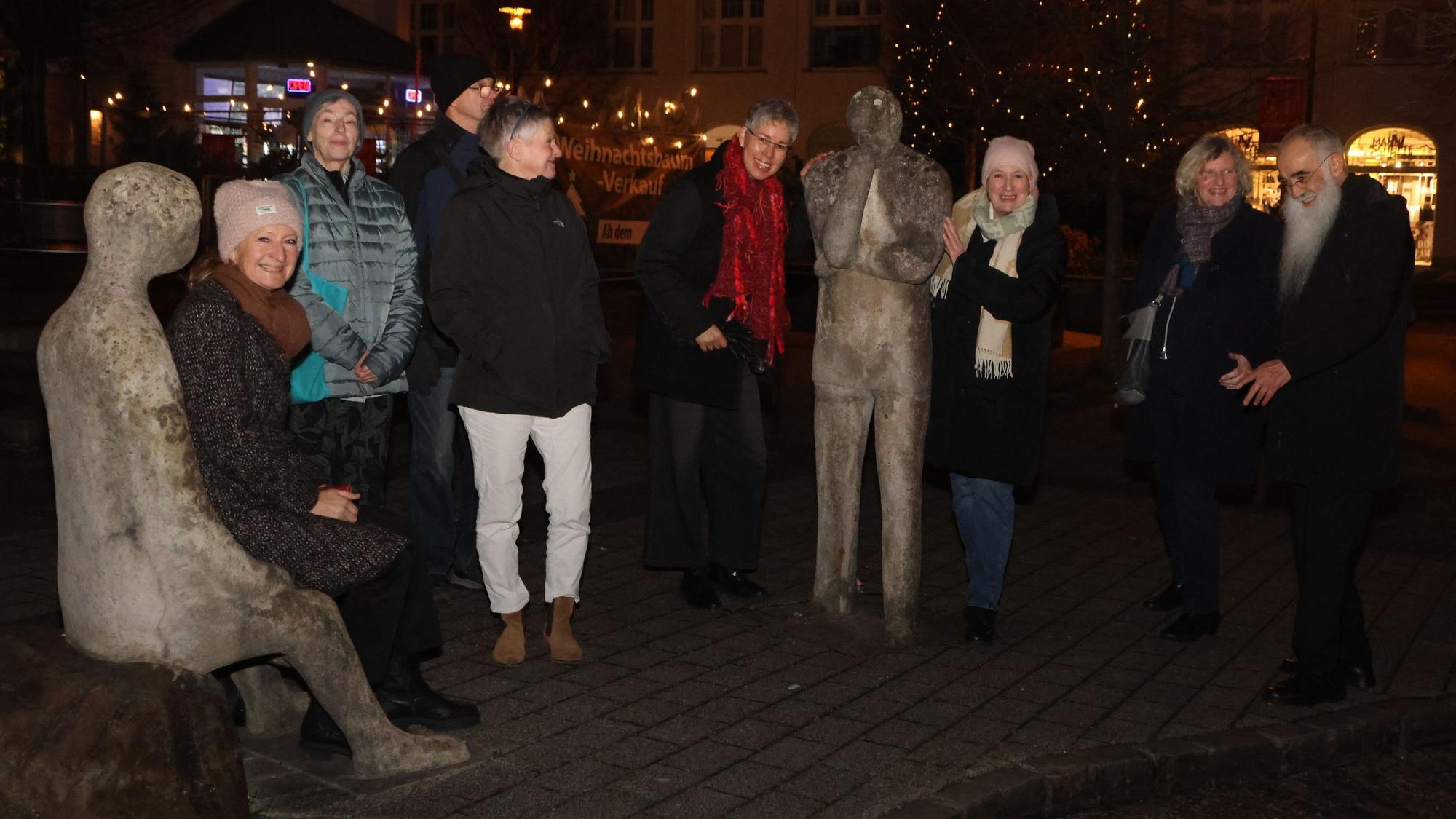 Eine Gruppe steht bei einem Spaziergang im Dunkeln zusammen an einer Skulpturengruppe.
