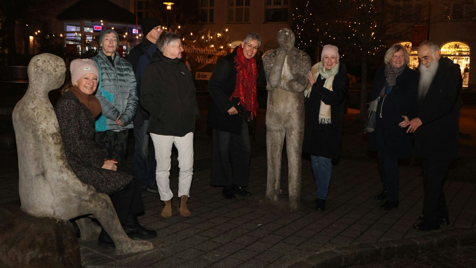 Eine Gruppe steht bei einem Spaziergang im Dunkeln zusammen an einer Skulpturengruppe.