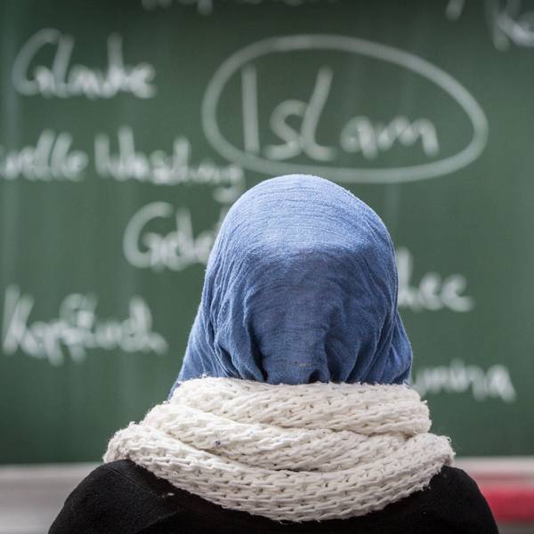 Eine Schülerin mit Kopftuch sitzt in einer Schule bei einer Unterrichtsstunde zum Thema Islam vor einer Tafel.