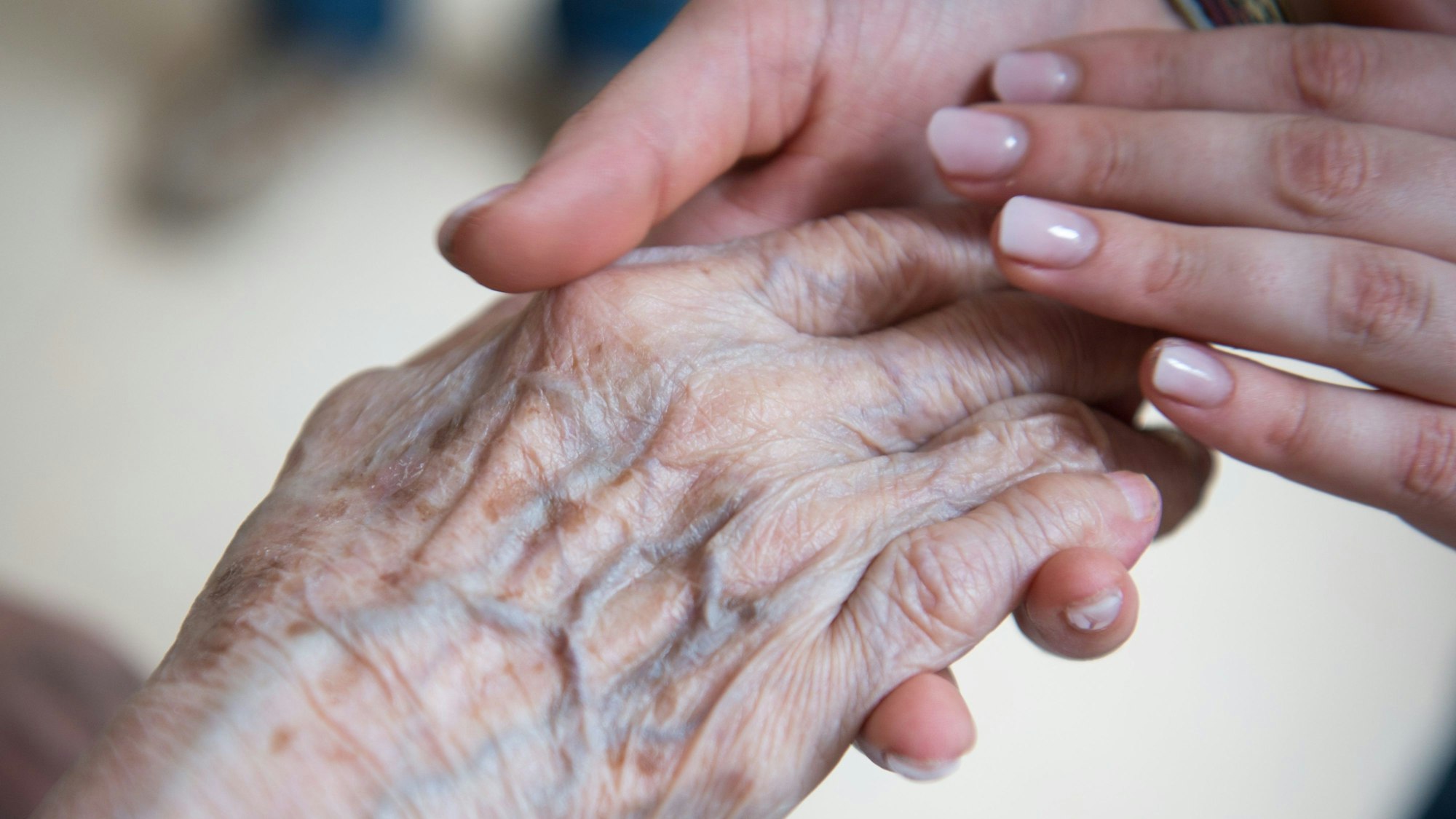 Eine jung Frau hält die Hand einer alten Frau.