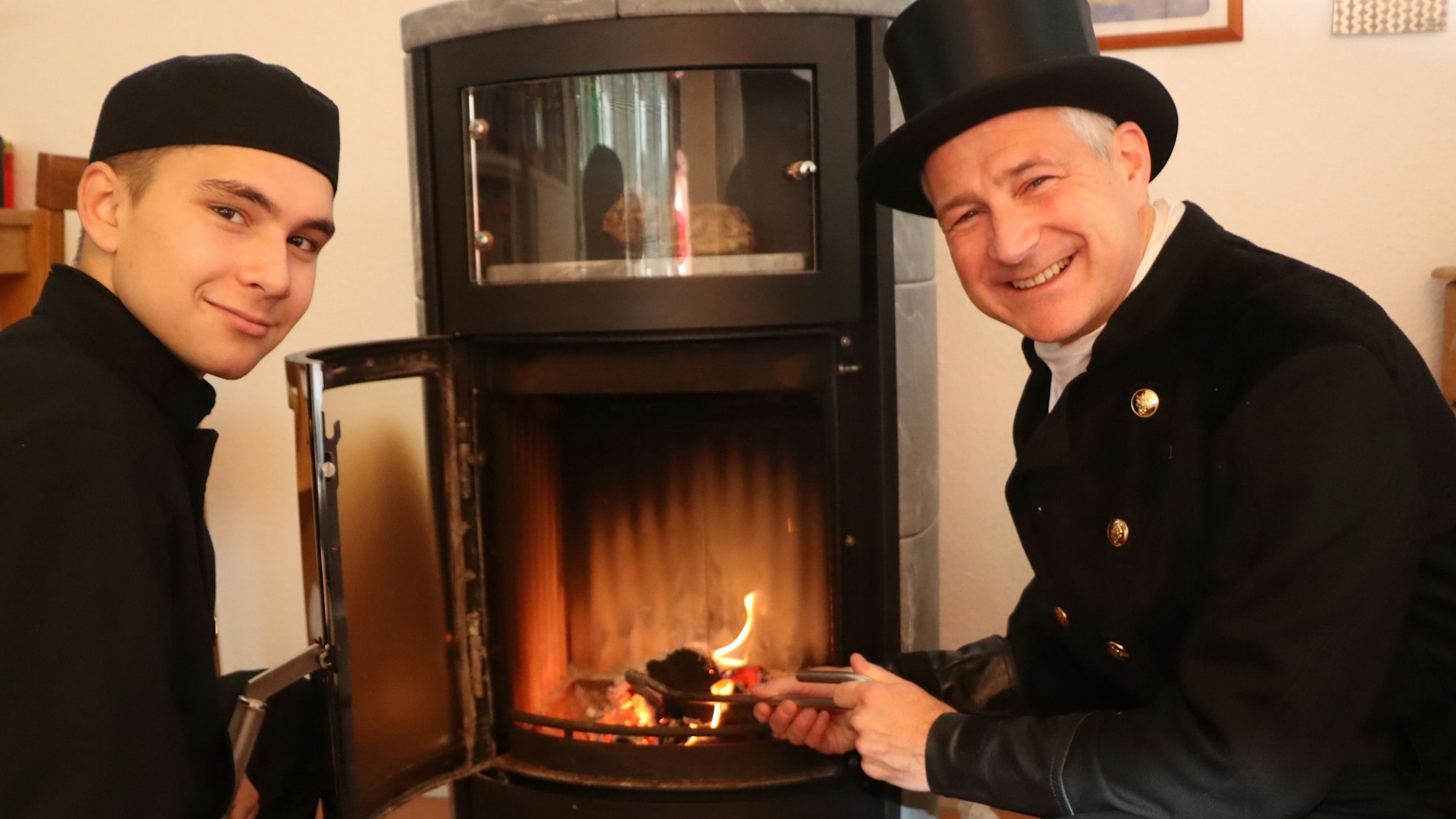 Zwei Schornsteinfeger sitzen vor einem Kamin.