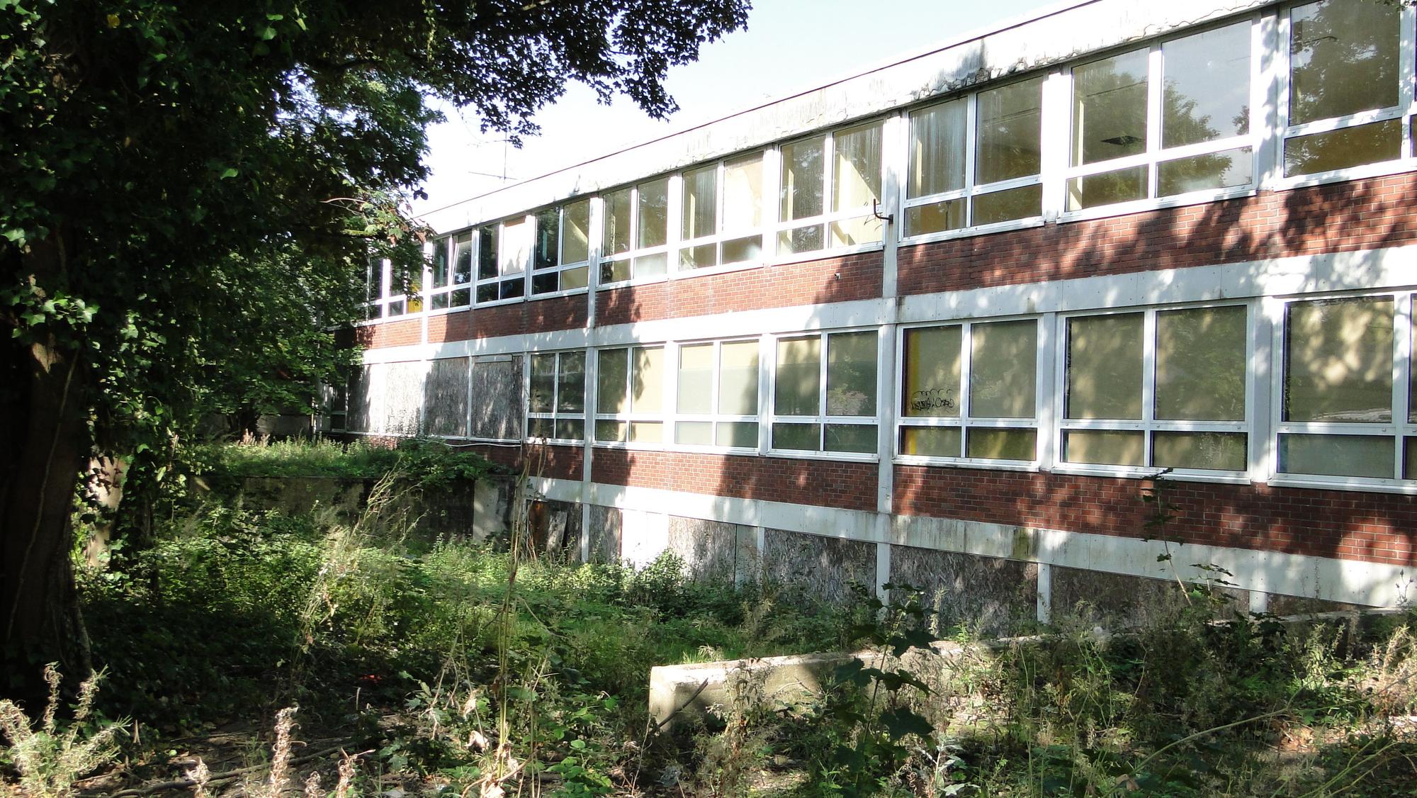 Blick auf ein dreigeschossiges Schulgebäude mit Sträuchern davor
