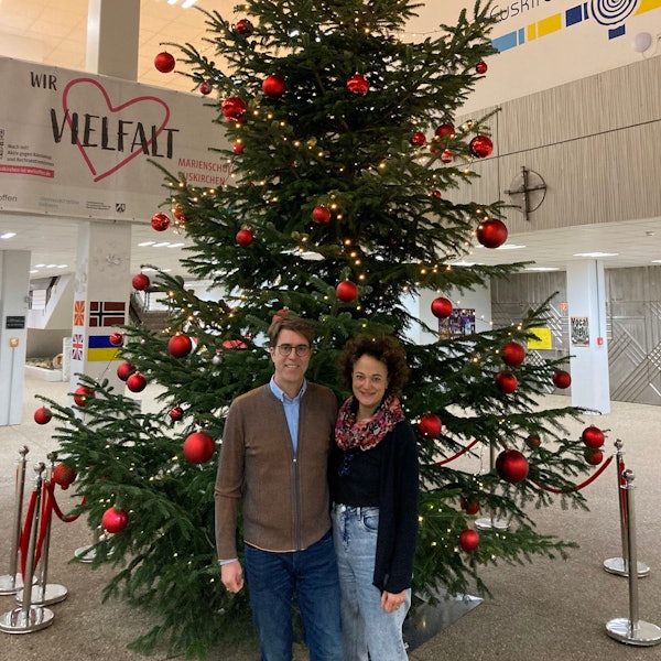 Michael und Barbara Luke stehen neben einem großen, mit roten Kugeln geschmückten Weihnachtsbaum.