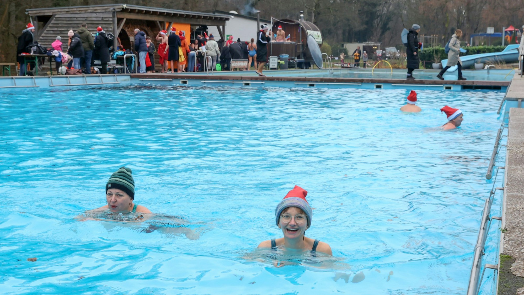 Zwei Frauen mit Mützen schwimmen in einem Außen-Schwimmbecken im Winter.