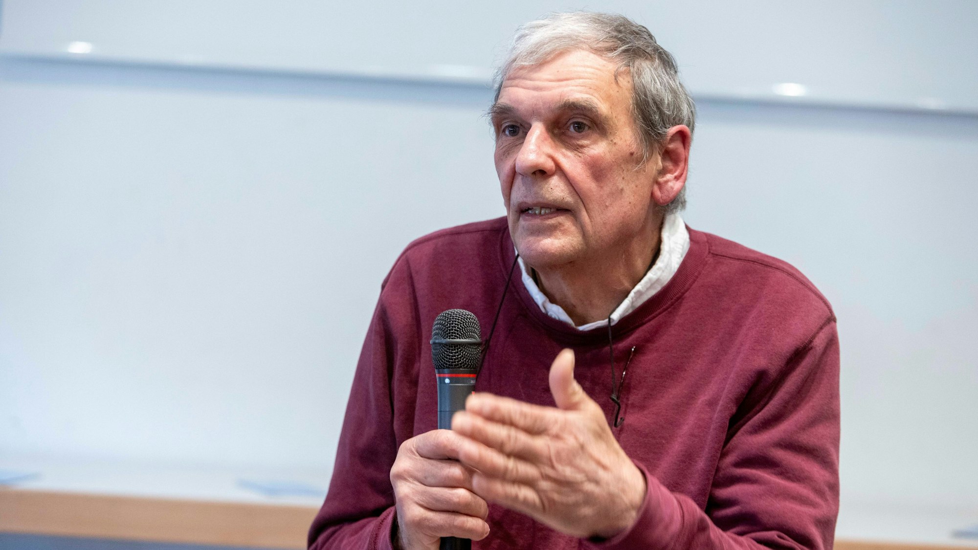Ein Mann in einem burgunderfarbenen Pulli spricht in ein Mikrofon.