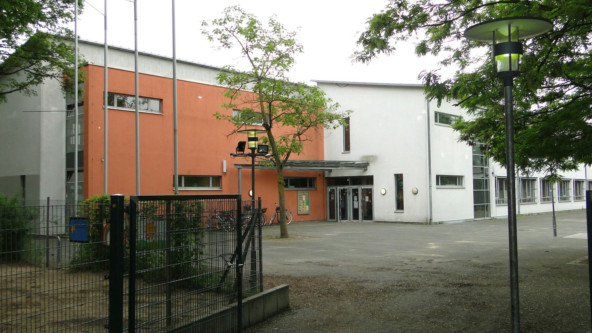 Blick auf eine Schule mit Schulhof und Bäumen davor