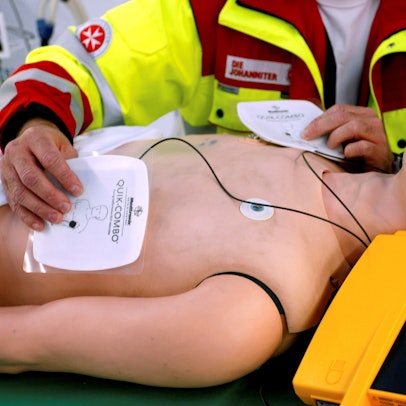 Ein Rettungssanitäter präsentiert einen öffentlich zugänglichen Defibrillator an einer Puppe.