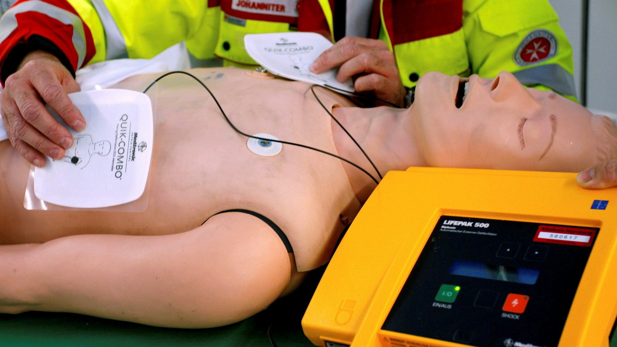 Ein Rettungssanitäter präsentiert einen öffentlich zugänglichen Defibrillator an einer Puppe.