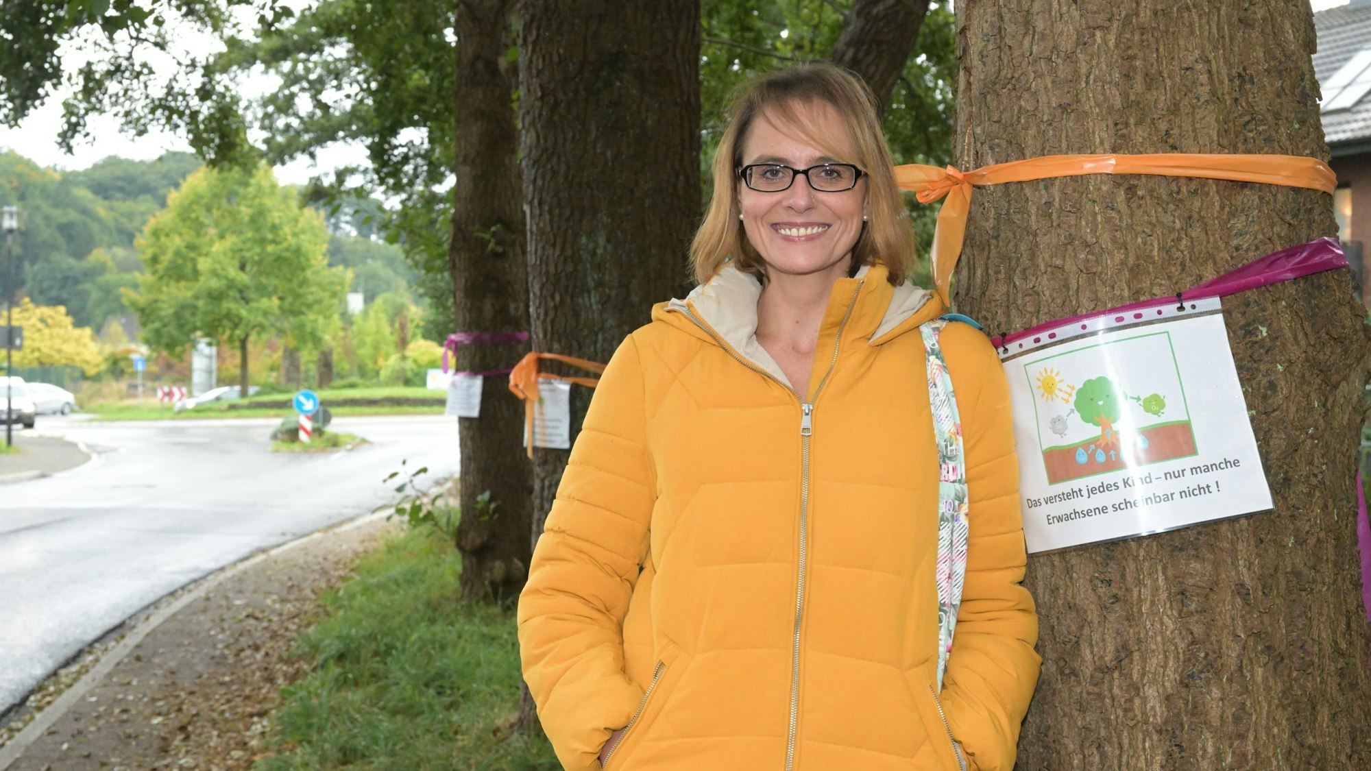 Eine Frau steht vor Bäumen, an deren Stämmen Protestschilder hängen.