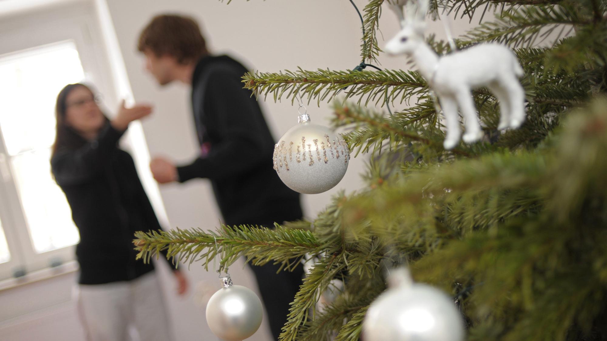 Ein Pärchen streitet sich am hinter einem geschmückten Christbaum.